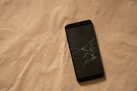 black phone with a cracked screen on a brown backgroundの写真素材