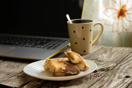 curd pancakes on a plate, a cup of tea and a laptop on a wooden tableの写真素材