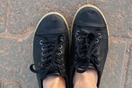 female legs in black sneakers in summer stand on the road a view from the topの写真素材