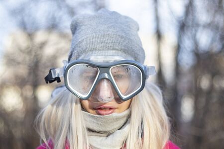 young girl is standing in a mask for diving in winter in the frost on the street, is waiting for a vacationの写真素材
