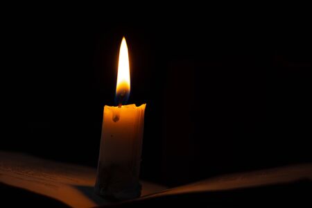 a burning candle stands on a book in a dark roomの写真素材