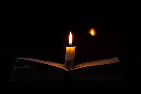 a burning candle stands on a book in a dark roomの写真素材