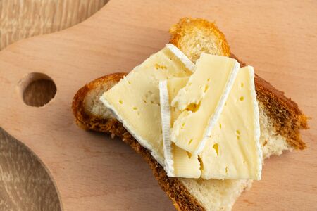 homemade bread and a piece of brie cheese on a wooden board in daylightの写真素材