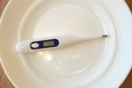 electronic thermometer lies on a white plate on the tableの写真素材