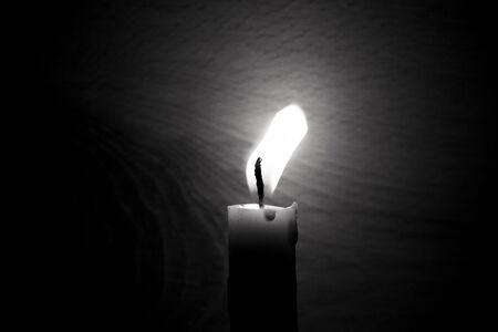 lighted candle stands in a dark room