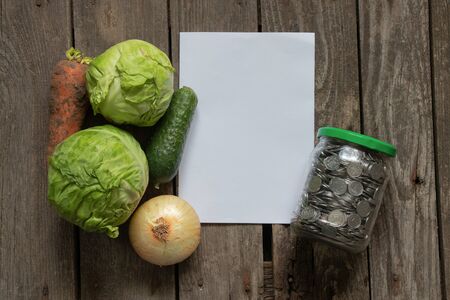 full can of Ukrainian coins and a vegetable set of cabbage carrots and onions on a table in the kitchen, price hike for vegetablesの写真素材