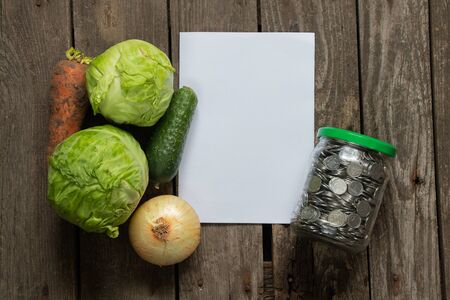 full can of Ukrainian coins and a vegetable set of cabbage carrots and onions on a table in the kitchen, price hike for vegetablesの写真素材