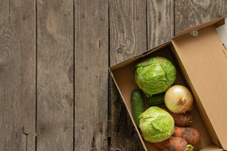 cabbage with cucumbers onions and carrots in a cardboard box on a wooden tableの写真素材