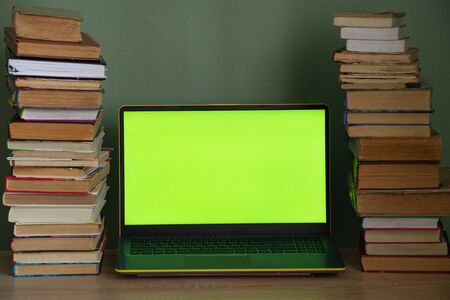 laptop green screen and a stack of books on the tableの写真素材