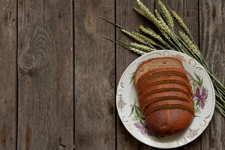 spikelets of wheat and a loaf of black sliced bread on an wooden stallの写真素材