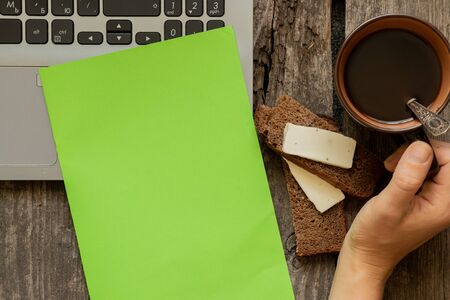 hand holds a cup of coffee a laptop sandwich and a blank green paper sheetの写真素材
