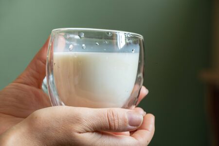 young Ukrainian girl holds a glass transparent cup with milk in the morningの写真素材