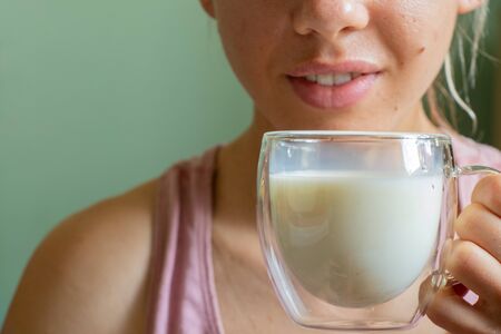 young Ukrainian girl holds a glass transparent cup with milk in the morningの写真素材