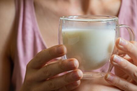 young Ukrainian girl holds a glass transparent cup with milk in the morningの写真素材