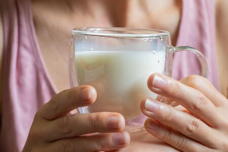 young Ukrainian girl holds a glass transparent cup with milk in the morningの写真素材