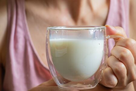young Ukrainian girl holds a glass transparent cup with milk in the morningの写真素材