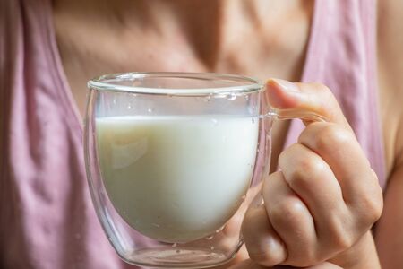 young Ukrainian girl holds a glass transparent cup with milk in the morningの写真素材