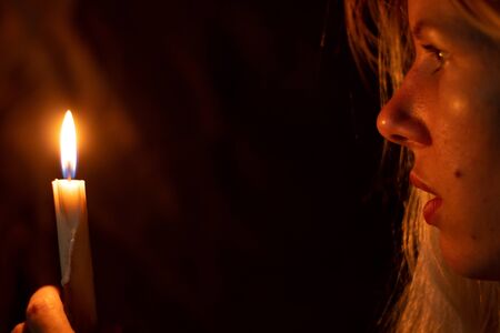 girl on a background of a burning candle in the dark prayingの写真素材
