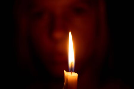 girl on a background of a burning candle in the dark prayingの写真素材