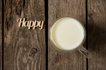 word happy in English from wooden letters and a glass with milk on a tableの写真素材