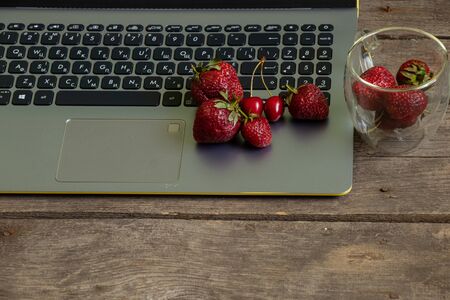 ripe strawberries and laptop on old wooden tableの写真素材
