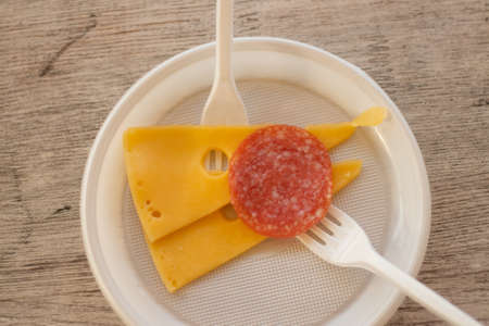 sliced cheese and sausage on a plastic plate with a fork on the table as a snackの写真素材