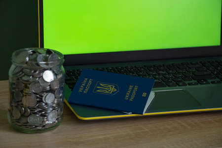 laptop with a green screen a penny in the bank and a passport on the table