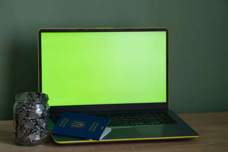laptop with a green screen a penny in the bank and a passport on the tableの写真素材