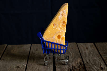 piece of cheese lies in a shopping trolley on a table on a dark backgroundの写真素材