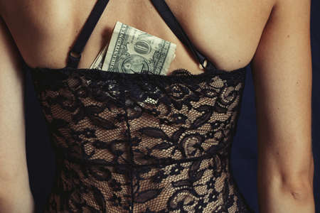 back of a young girl in lace black lingerie close up on an isolated background and dollar bills are embedded in lingerieの写真素材