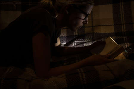 girl in the dark in the bedroom reads a book on the sofaの写真素材