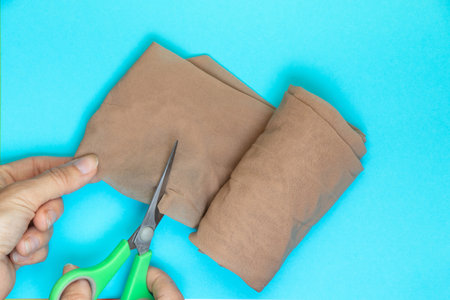 female hands cuts nylon tights with scissors on a blue background close-upの写真素材
