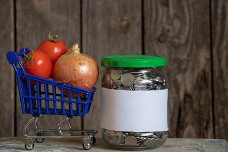 jar with Ukrainian pennies with a white sheet of paper and a blue basket with vegetables on a wooden tableの写真素材