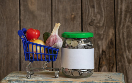 jar with Ukrainian pennies with a white sheet of paper and a blue basket with vegetables on a wooden tableの写真素材
