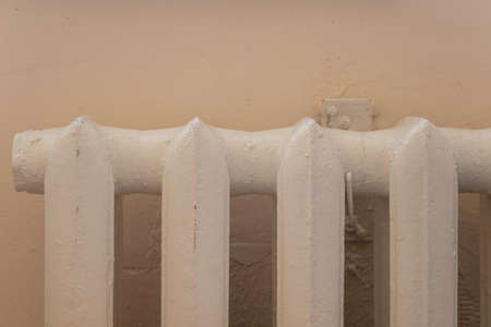cast iron old white battery on a beige wall closeup