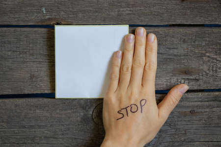 white sheet of paper paper and next to hand with the inscription stop on a wooden table, place for textの写真素材