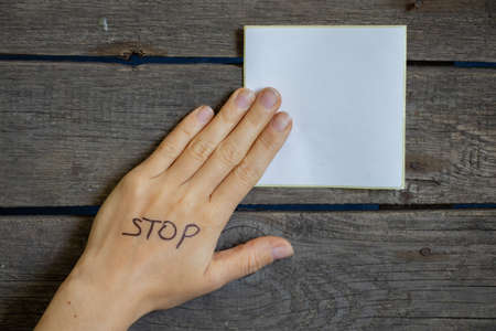 white sheet of paper paper and next to hand with the inscription stop on a wooden table, place for...