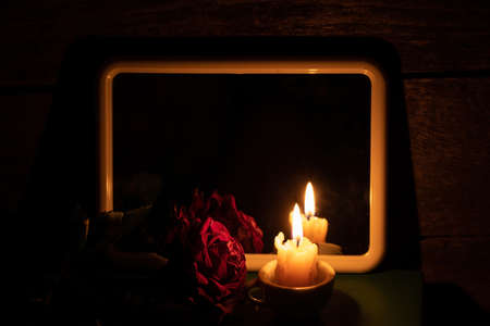 dry rose and candle flame poured mirrors on the table in the dark in the room, occult theme