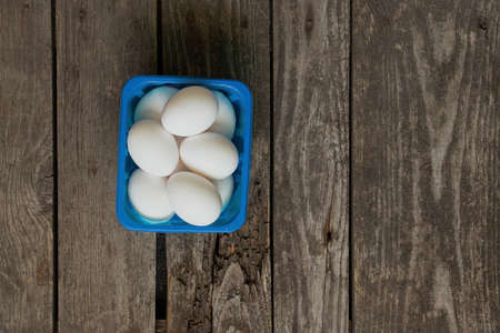 white chicken eggs in a blue box on a wooden table in the kitchenの写真素材