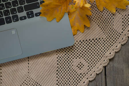 gray laptop lies on a brown lace napkin on a wooden table and a yellow autumn oak branch, laptop on the table, autumn moodの写真素材