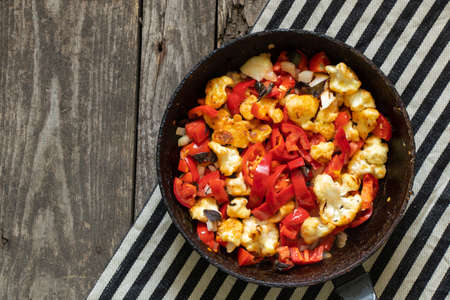 cauliflower with tomatoes and peppers stewed in a pan is on the table in the kitchen, no meat, vegan foodの写真素材