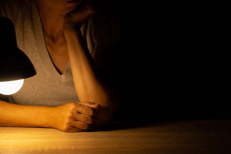 girl sitting at a table in the light of a table lamp in a dark room