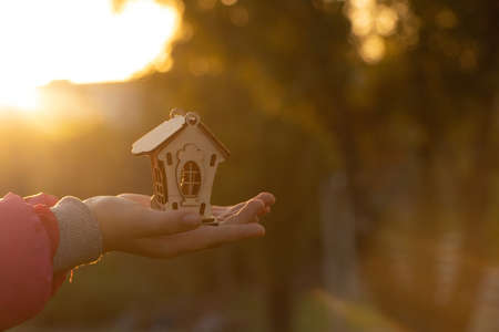 hands hold a small wooden house against the background of the sun at sunset, dream houseの写真素材