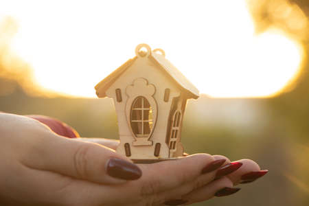 hands hold a small wooden house against the background of the sun at sunset, dream house