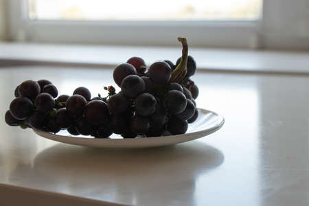 ripe grapes lies on a white plate on a white table in the kitchen