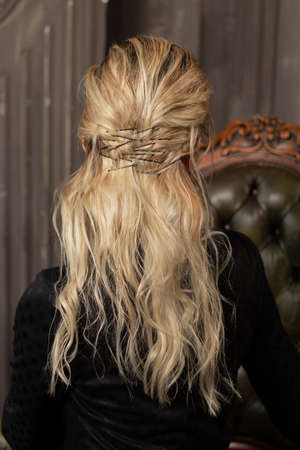 blonde long curly hair with hairpins on model on isolated dark background close-up in studio, back...