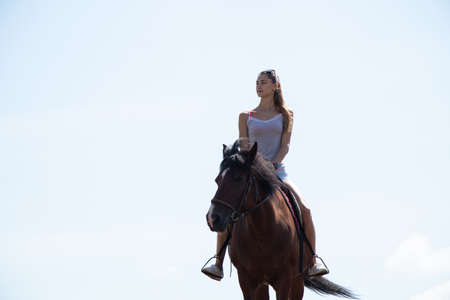 girl sitting on horseback against the sky on a sunny day