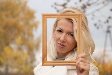 portrait of a blonde young girl in an empty wooden frame on the street in the autumn afternoon in the parkの写真素材