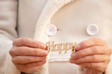 happy word in english made of wooden letters in the hands of a girl on the street during the dayの写真素材
