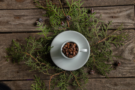 white cup full of whole roasted coffee beans stands on branches with a christmas tree on the table, new year designの写真素材